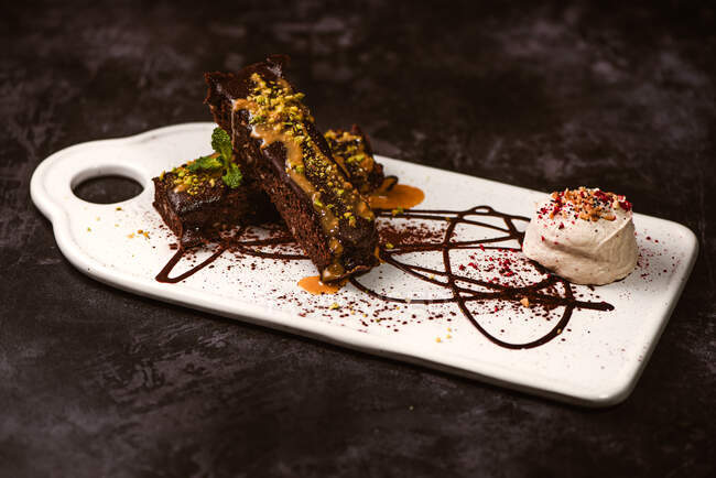 Leckere Brownies mit Erdnussbutter und knusprigen zerdrückten Pistazien in der Nähe von Eislöffel auf Teller mit Schokoladensauce — Stockfoto