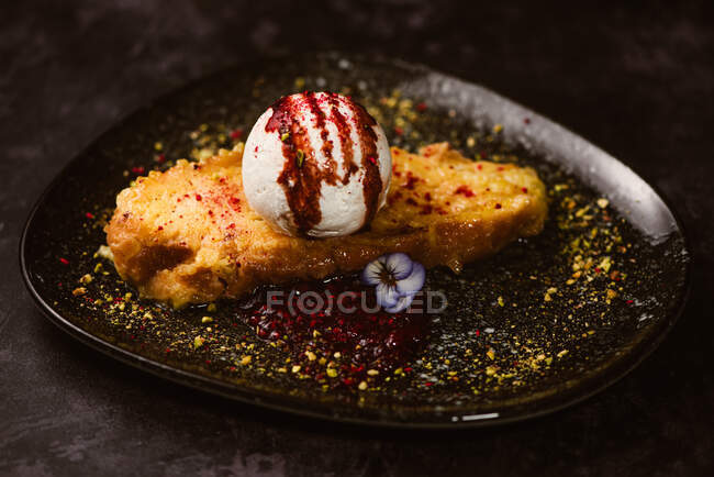 Yummy French toast with meringue milk ice cream scoop covered with sweet berry sauce on plate with condiments in restaurant on dark background — Stock Photo