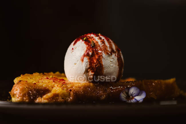 Low angle view of yummy French toast with meringue milk ice cream scoop covered with sweet berry sauce on plate with condiments in restaurant on dark background — Stock Photo