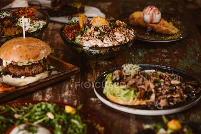 Appetitliche vegetarische Gerichte mit sautierten Pilzen und Gemüse in der Nähe von Burger und Eis mit French Toast auf Holztisch — Stockfoto