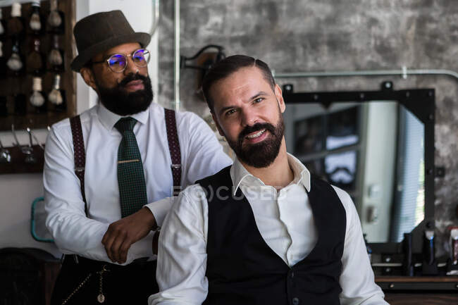 Cheerful adult male entrepreneur with masculine mature ethnic beauty master in formal clothes in barbershop — Fotografia de Stock