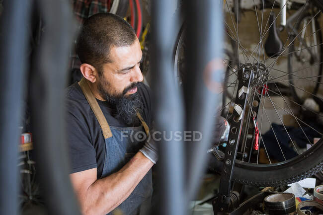 Серйозний дорослий чоловік в фартусі і рукавичках ремонтує колесо мотоцикла в сучасному гаражі — стокове фото