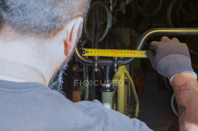 Crop unrecognizable bearded male mechanic in gloves measuring handlebar while repairing bicycle in garage — Stock Photo