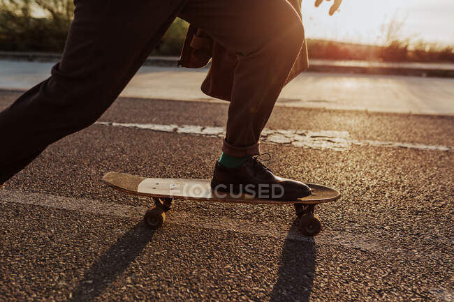 Cropped anonymous male skater in stylish wear riding skateboard along asphalt road in countryside - foto de stock