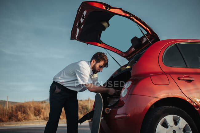 Side view of young bearded male driver with opened car trunk getting dressed — Foto stock