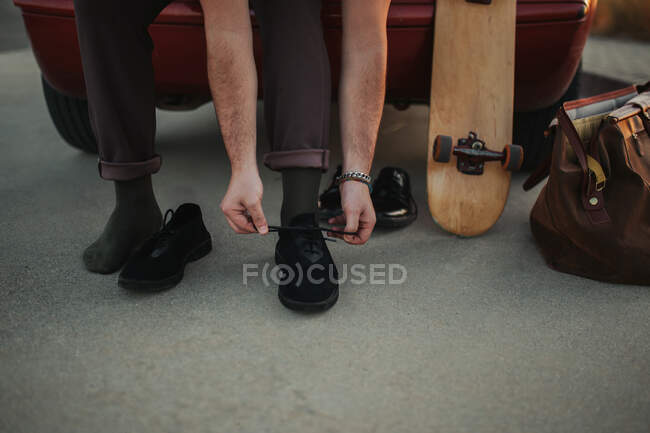 Von oben nicht wiederzuerkennende männliche Skater sitzt auf dem Kofferraum in der Nähe Tasche und schnürt Schnürsenkel beim Umziehen Skateboard fahren — Stockfoto