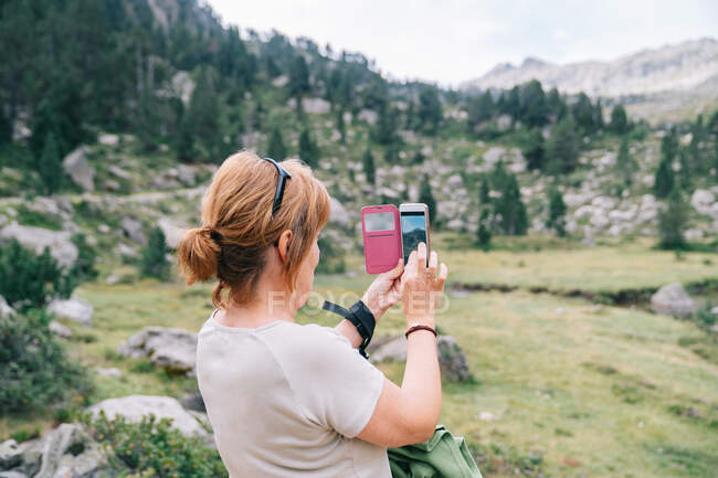 Back view anonymous female taking pictures on smartphone of amazing stony verdant highlands in Ruda Valley in Catalan Pyrenees — Foto stock