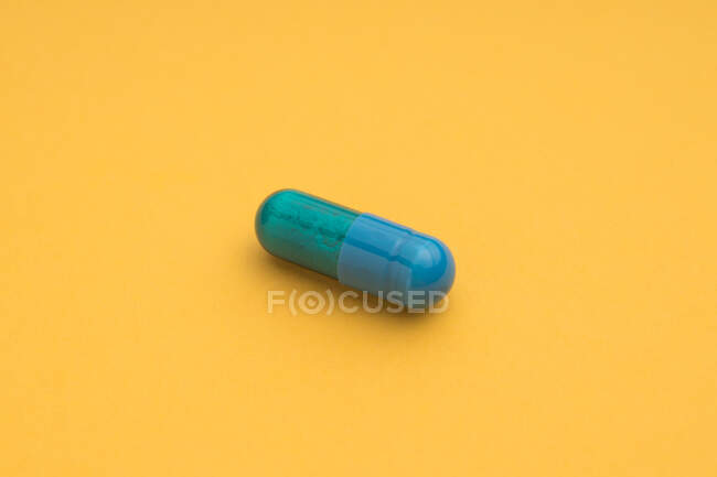 Високий кут блакитної капсули фармацевтичного препарату, поміщений на яскраво-жовтому тлі. — стокове фото