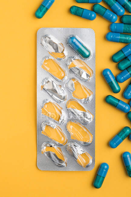 Сверху пластиковые блистерные упаковки с голубыми медицинскими капсулами размещены на желтом фоне — стоковое фото