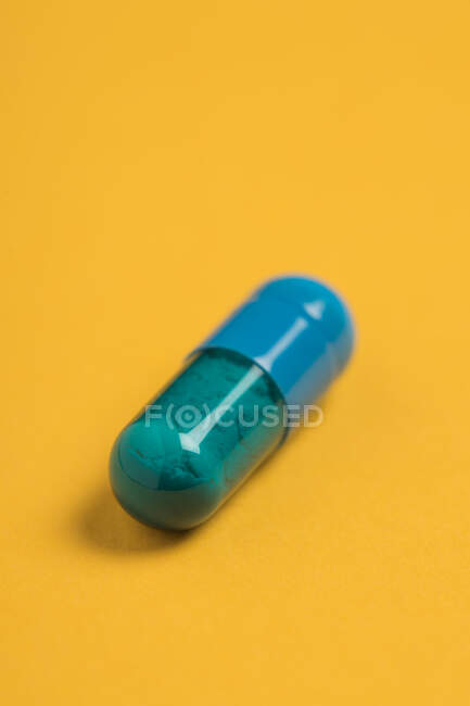 Ângulo elevado da cápsula azul do medicamento farmacêutico colocada sobre fundo amarelo brilhante — Fotografia de Stock