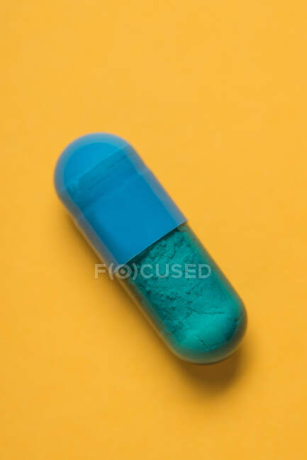 High angle of blue capsule of pharmaceutical medicinal product placed on bright yellow background — Stock Photo