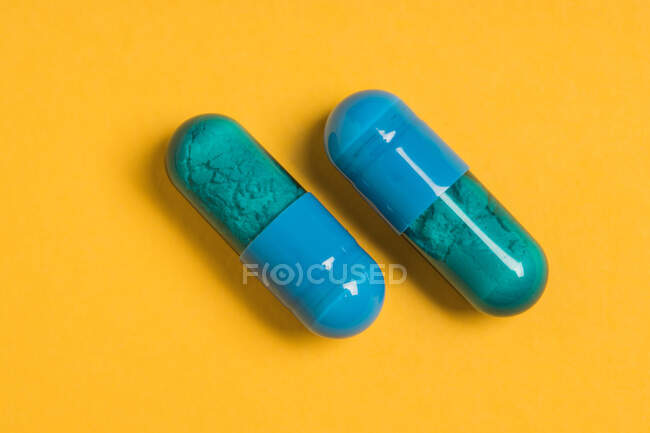 Grand angle de capsules bleues de médicament pharmaceutique placées sur fond jaune vif — Photo de stock
