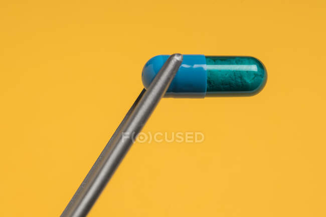 Високий кут блакитної капсули фармацевтичного препарату, поміщений на яскраво-жовтому тлі. — стокове фото