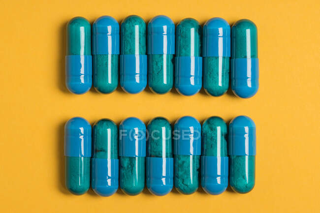 Vue du dessus des capsules en plastique remplies de remède lumineux pour le traitement médical sur fond jaune — Photo de stock