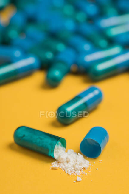 Ângulo alto do conteúdo da droga médica derramada fora da cápsula colorida azul no fundo amarelo — Fotografia de Stock