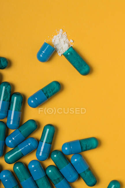 Високий кут вмісту лікарських препаратів вилитий з блакитної капсули на жовтому тлі. — стокове фото