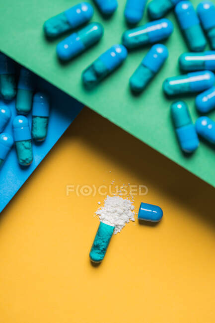 High angle of contents of medical drug poured out of blue colored capsule on yellow background — Stock Photo