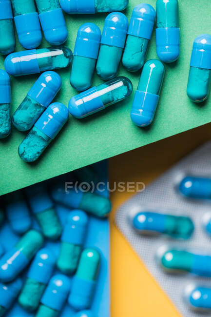 З верхнього боку пластикові пухирці з блакитними медичними капсулами, розміщеними на жовтому і зеленому і синьому фоні. — стокове фото