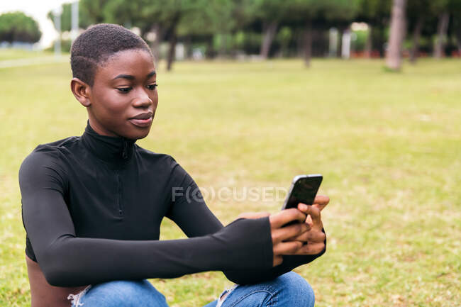 Junge ethnische Frau in lässiger Kleidung mit drahtlosem Headset, die Selbstporträt auf Handy im Park macht — Stockfoto