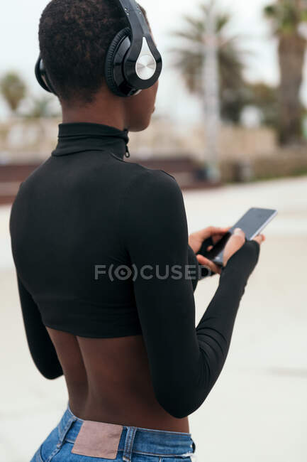 Vue arrière messagerie texte ethnique féminine sur téléphone portable avec écran noir en ville — Photo de stock