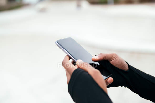 Recortar mensajes de texto femeninos étnicos anónimos en el teléfono móvil con pantalla negra en la ciudad - foto de stock