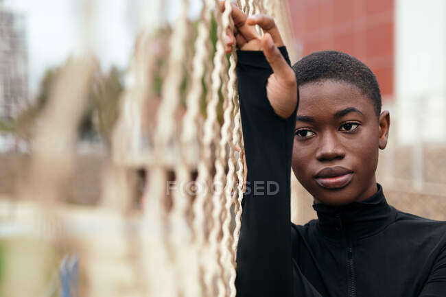 Jeune femme ethnique poignante aux cheveux courts en vêtements décontractés regardant loin en ville à la lumière du jour — Photo de stock