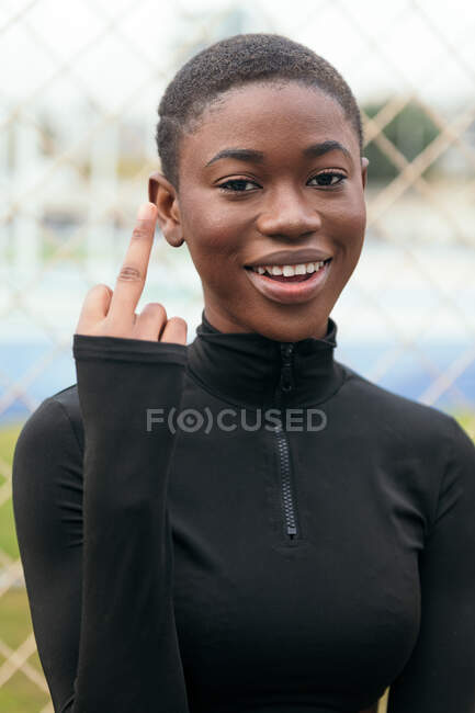 Smiling young African American female with stretched arm demonstrating fuck gesture in town on summer day - foto de stock