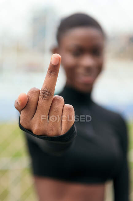 Smiling young African American female with stretched arm demonstrating fuck gesture in town on summer day — Fotografia de Stock