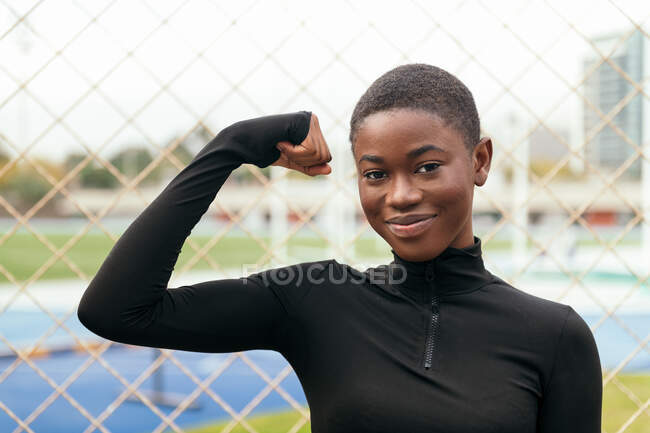 Jovem conteúdo afro-americano feminino com cabelo curto olhando para a câmera enquanto levanta o braço na cidade — Fotografia de Stock