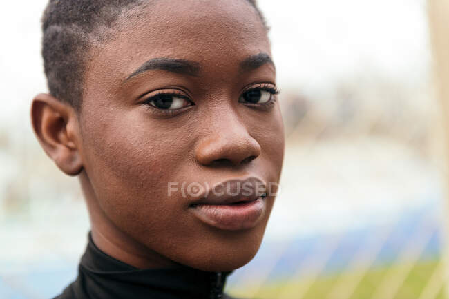 Giovane tenera femmina etnica in abito nero con i capelli corti guardando la fotocamera sul prato urbano in estate — Foto stock