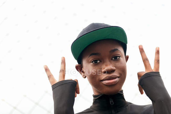 Baixo ângulo de jovem afro-americana em desgaste casual olhando para a câmera com o dedo para cima à luz do dia — Fotografia de Stock