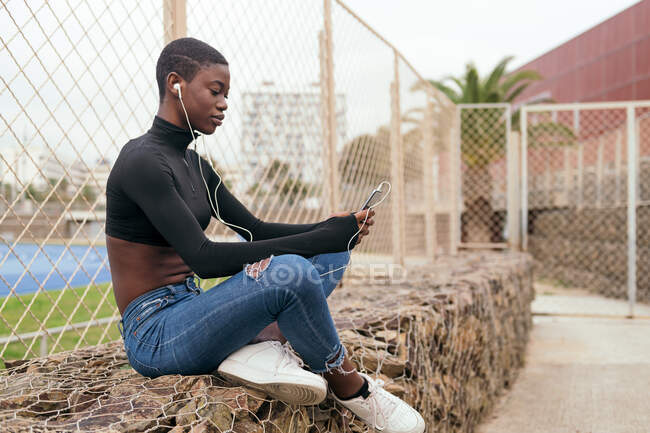 Короткошерстная черная женщина слушает музыку с помощью мобильного телефона и наушников — стоковое фото