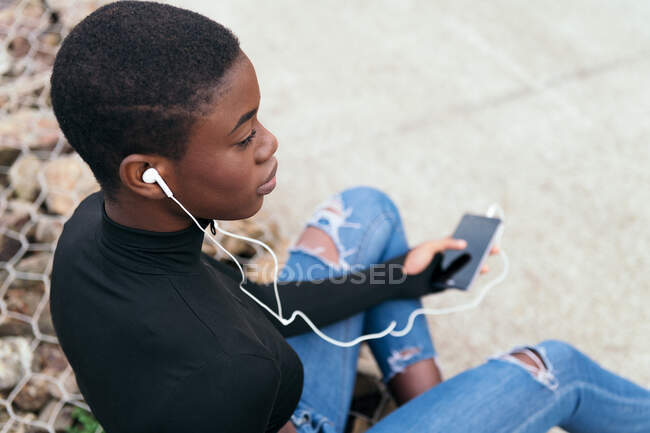 Femme noire aux cheveux courts écoutant de la musique avec un téléphone portable et un casque — Photo de stock