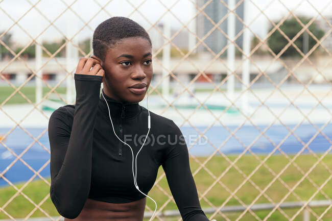 Mujer negra de pelo corto escuchando música con un teléfono móvil y auriculares - foto de stock