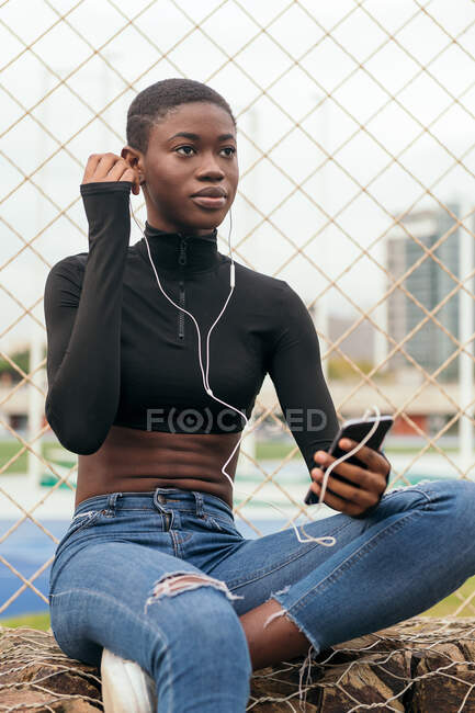 Kurzhaarige schwarze Frau hört Musik mit Handy und Kopfhörer — Stockfoto