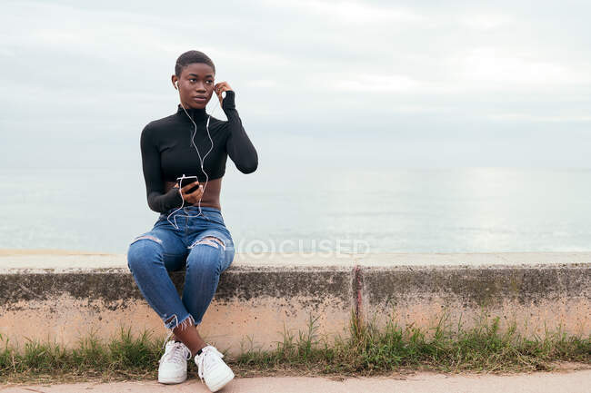 Donna nera dai capelli corti che ascolta musica con telefono cellulare e cuffie — Foto stock
