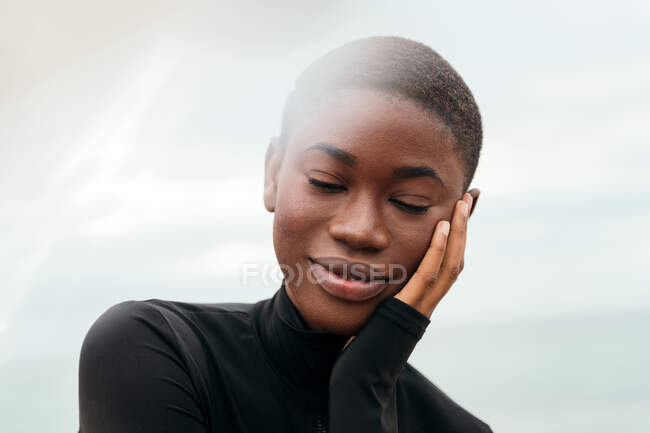 Junge kontemplative ethnische Frau mit geschlossenen Augen und kurzen Haaren berührt Gesicht bei Tageslicht — Stockfoto
