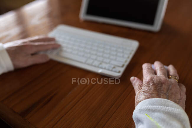 Cortar paciente anônimo com teclado contra tablet com médico na tela durante videochamada em casa — Fotografia de Stock