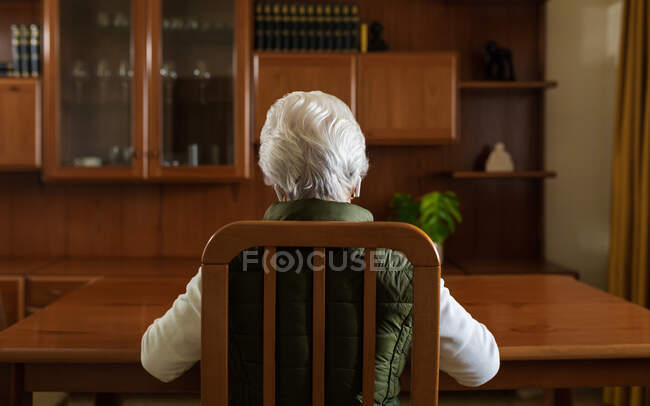 Back view of anonymous elderly female patient in TWS earbuds speaking with doctor on tablet during video call at home — Stock Photo