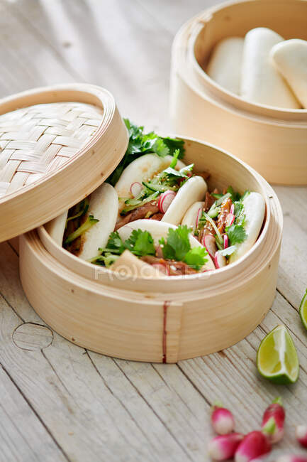 From above of tasty steamed baozi buns with radish and cucumber slices with meat and fresh cilantro on table — Stock Photo
