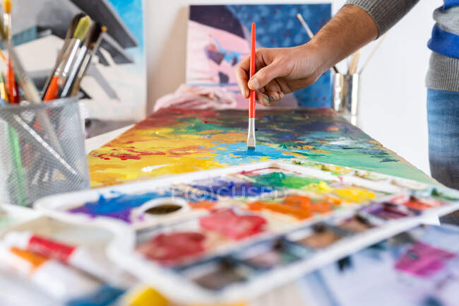 Récolter peintre masculin méconnaissable en utilisant un pinceau professionnel pendant le processus de peinture sur feuille de carton près des outils d'art dans la salle de travail — Photo de stock