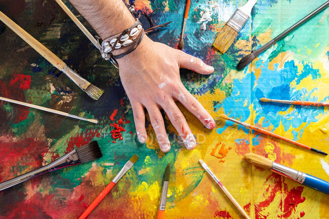 Top view of crop anonymous male painter with collection of professional tools on bright painted picture — Stock Photo