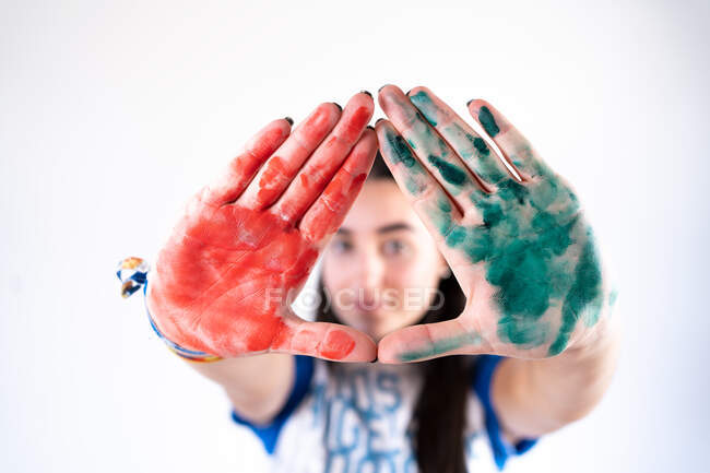 Young female artist looking at camera with stretched arms with red and green paints on palms of hands — Fotografia de Stock