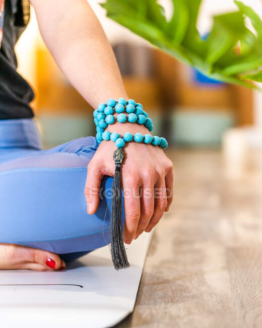 Cropped unrecognizable female in activewear sitting on mat on Half Lotus meditating with mala beads on arm in light studio — Stock Photo