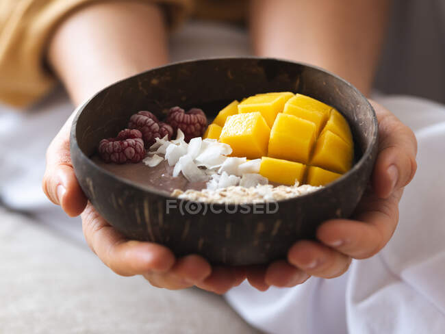 Crop anonymous female holding power bowl with fresh tasty mango and coconut chips in daytime — Stock Photo