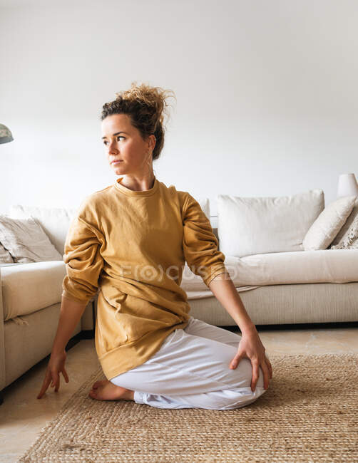 Vista laterale di femmina calma in abbigliamento sportivo seduto sul pavimento in posa vajrasana durante la pratica dello yoga a casa — Foto stock