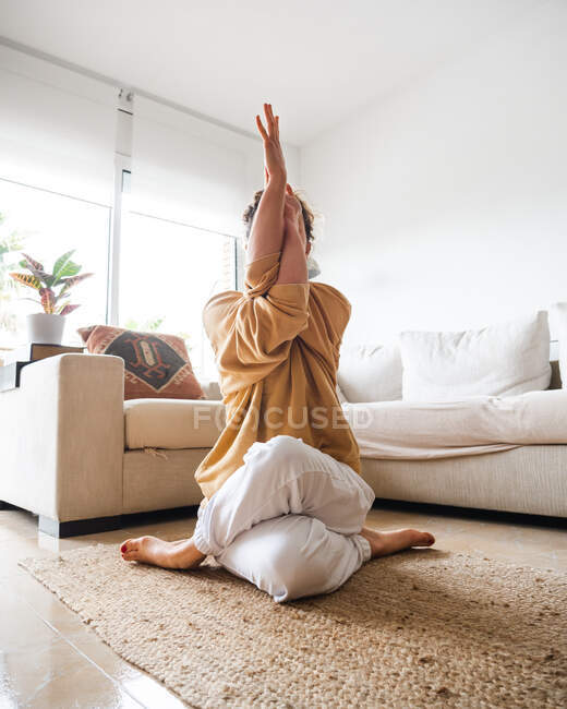 Calma donna irriconoscibile in abbigliamento sportivo seduta sul tappeto sul pavimento e che esegue Garudasana durante la pratica dello yoga a casa — Foto stock