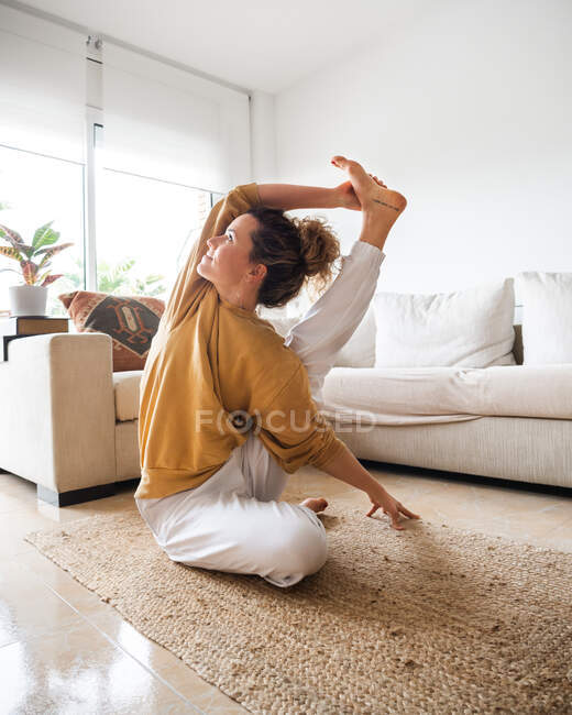Donna calma in abiti casual seduta sul pavimento e che esegue Surya Yantrasana asana durante la pratica dello yoga in soggiorno leggero a casa — Foto stock