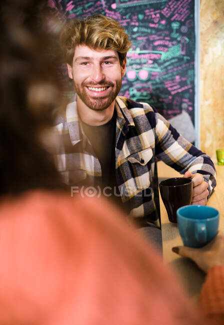Jeune couple joyeux en vêtements décontractés lumineux parlant dans la cuisine confortable et se regardant tout en prenant un café — Photo de stock