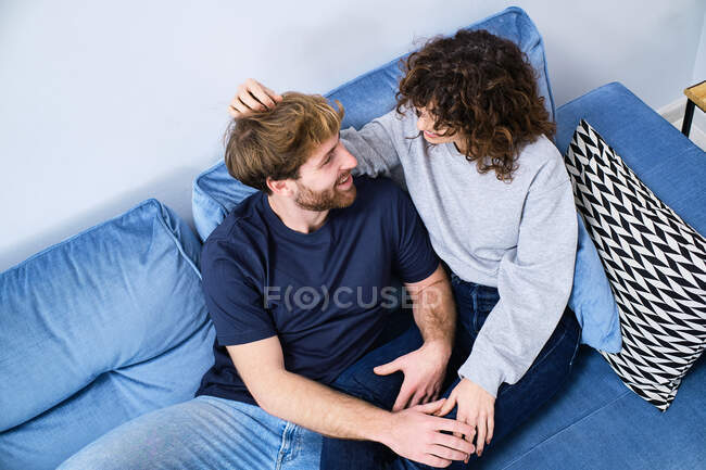 From above happy young couple in casual clothes sitting on couch and looking at each other while spending time together — Stock Photo
